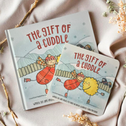 A board book edition of The Gift of a Cuddle, with a gentle cover illustration of a parent and child sharing a cuddle beneath stars.
