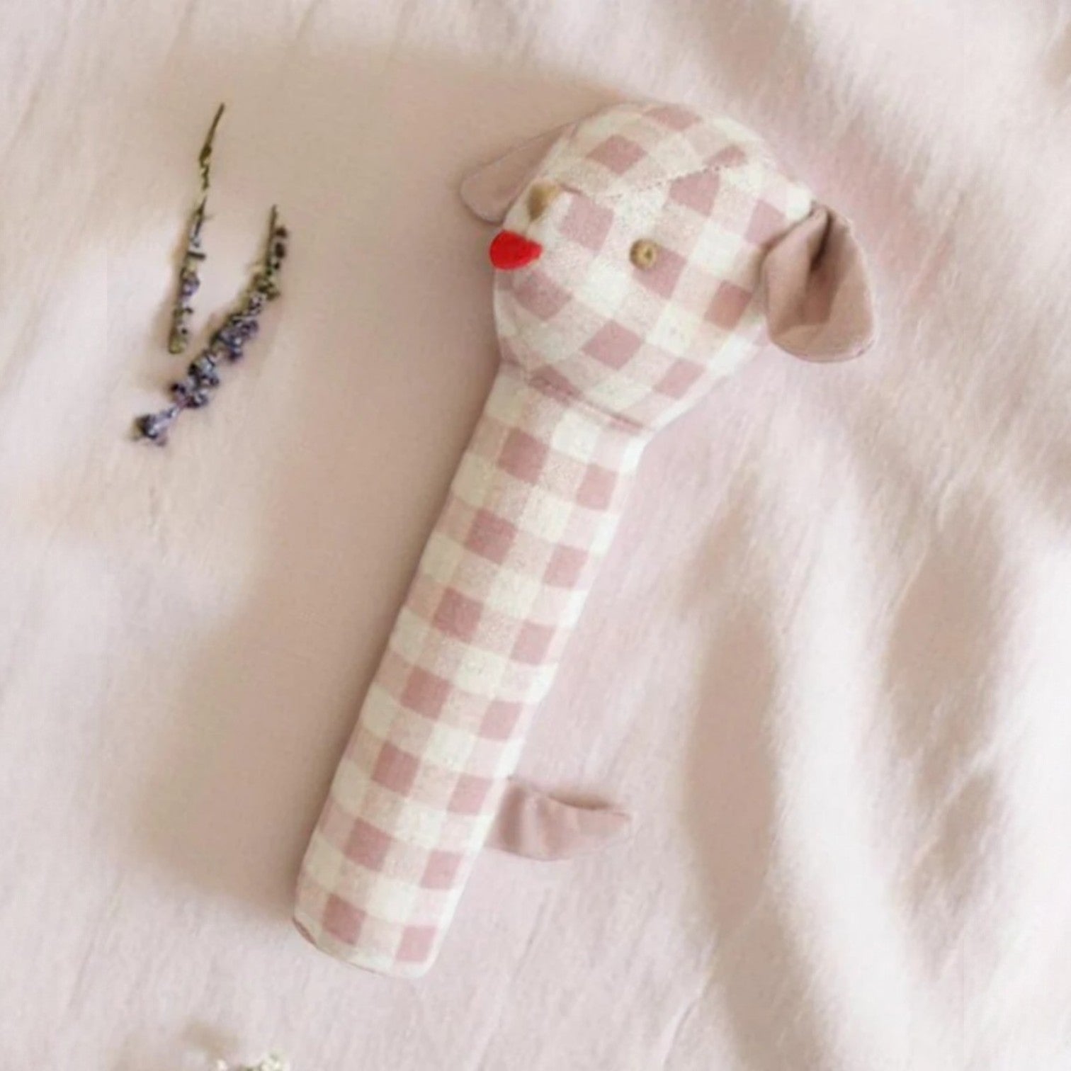 A rose check linen puppy-shaped baby squeaker toy with stitched features, resting against a soft, neutral background.