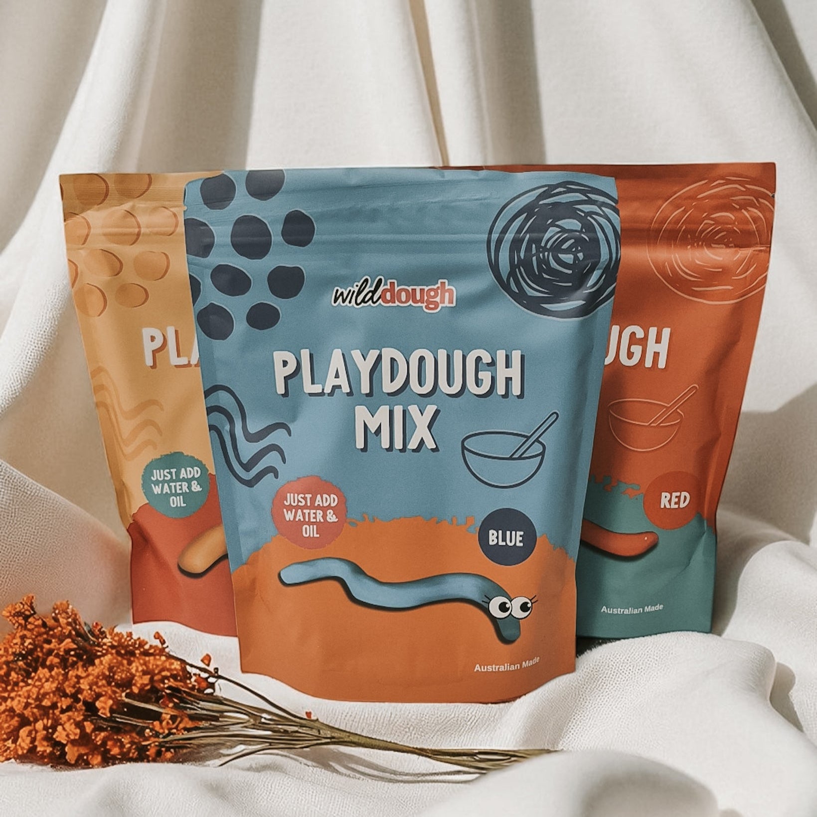 Three packages of wilddough Playdough Mix on a white background with dried flowers.