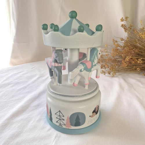 A pastel wooden musical carousel featuring white and mint horses with blush details, photographed against a neutral linen backdrop with dried wildflowers for a soft, vintage-inspired aesthetic.